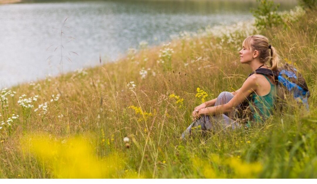 Woman sitting in long grass, symbolising calm and relief from overstimulation as a Highly Sensitive Person (HSP)